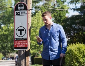 A young male sighted volunteer entering clues into the BlindWays App next to a bus stop sign.
