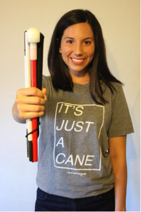 Ashley Broussard wearing her "It's Just a Cane" t-shirt and holding out a white mobility cane