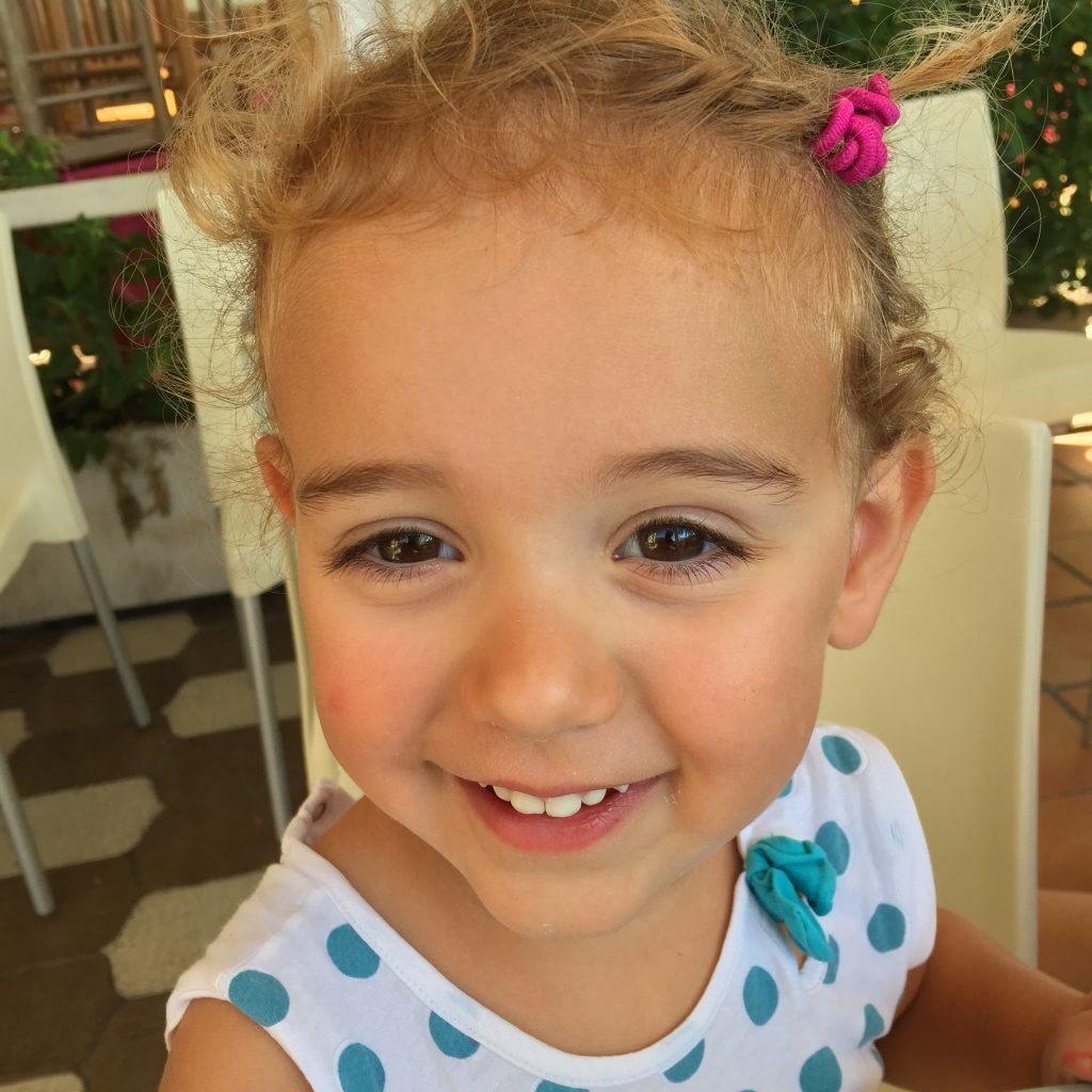 Four-year-old Vicky, wearing a white shirt with blue polka dots, smiles for the camera