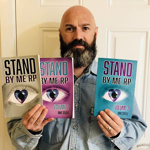 Dave Steele looks at the camera while holding his three books, Stand By Me RP (volumes 1, 2 and 3)