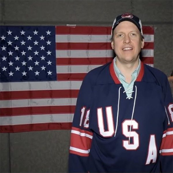 Doug Goist, wearing a USA jersey, smiles for the camera in front of an American flag