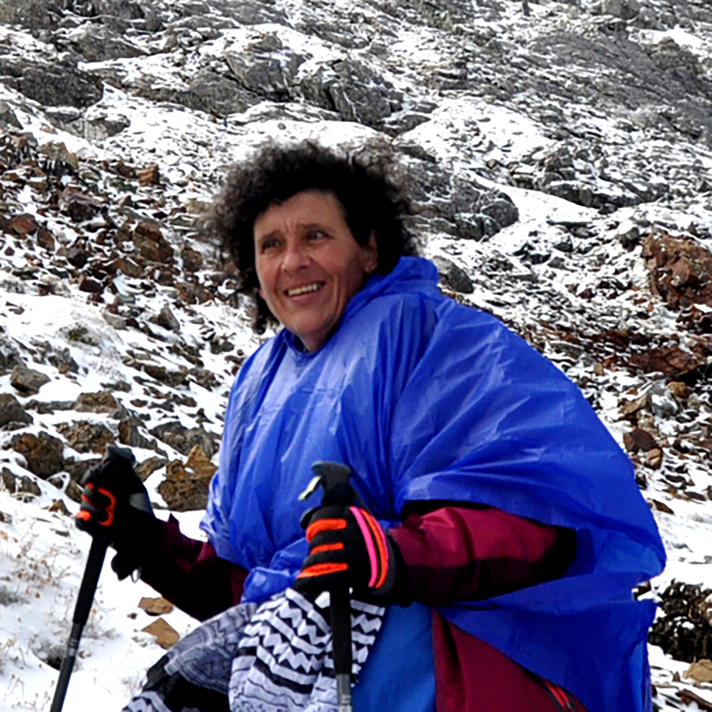 Julia - wearing a blue parka and red gloves - smiles as she makes her way to the summit