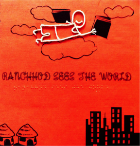 The cover of the first prototype of "Ranchhod Sees the World." The cover is red with the title printed in black text and imprinted in braille. There is an illustration of a village and a city and a tactile outline of a boy - made of string - is flying through the clouds above.