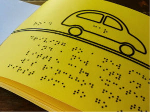 A bright-yellow page imprinted with black braille and a tactile illustration of a small car.