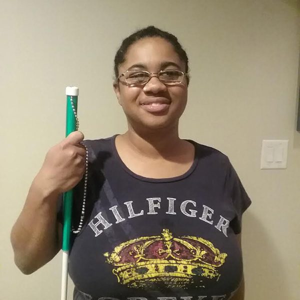 Jasmyn smiles at the camera while holding her cane.
