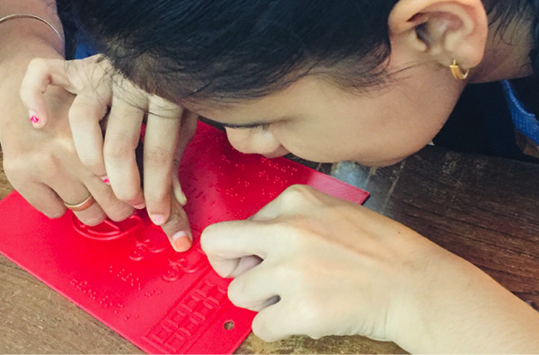 With the guidance of a teacher, a child touches the tactile illustration in a Beyond Braille book.