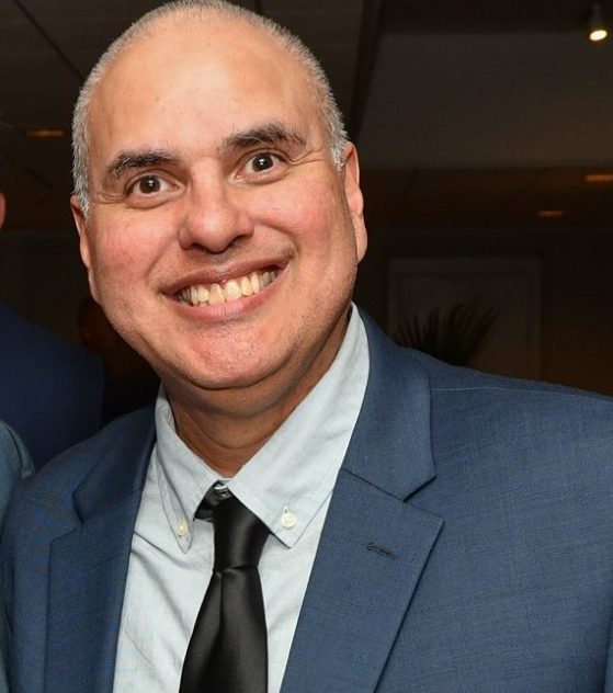 Deafblind actor Robert Tarango, star of Oscar-nominated Feeling Through, wearing a suit and tie, smiles broadly for the camera in a close-up photo