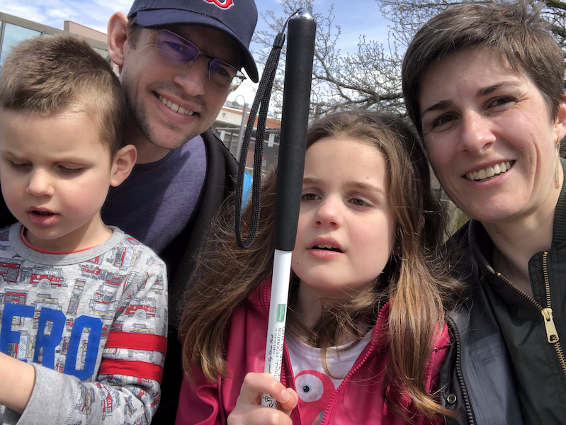 A selfie of Jolandi with her husband and two children, Daniel and Hannah. All are smiling and Hannah holds a white mobility cane high in front of her.