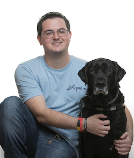 Chad, wearing a t-shirt with the word "hope" on the chest, kneels alongside Andros, his black Lab guide dog