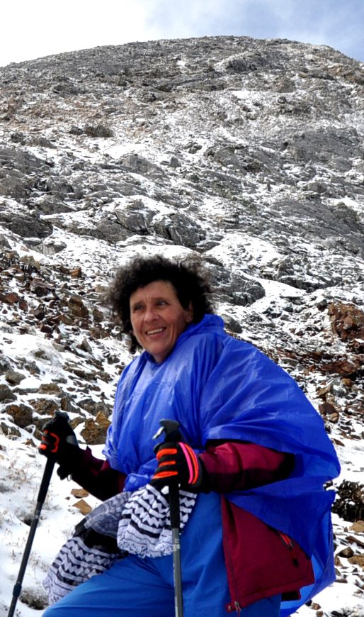 Julia - wearing a blue parka and red gloves - smiles as she makes her way to the summit