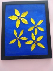 This painting has four big yellow flowers on a blue background. The flowers are made of dry leaves and golden beads. 