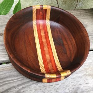 Small bowl with medium color wood, has red and yellow striped wood laminated through the middle. 