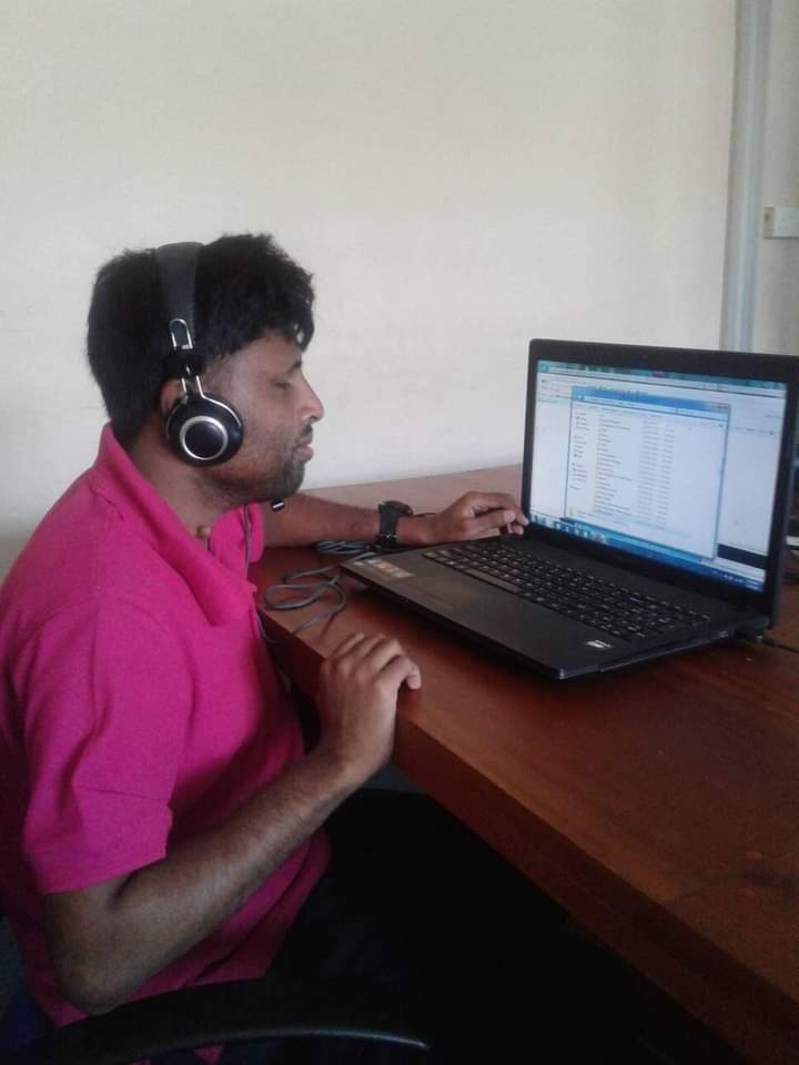 Palitha, wearing a headset, sits at a desk and works on a laptop computer