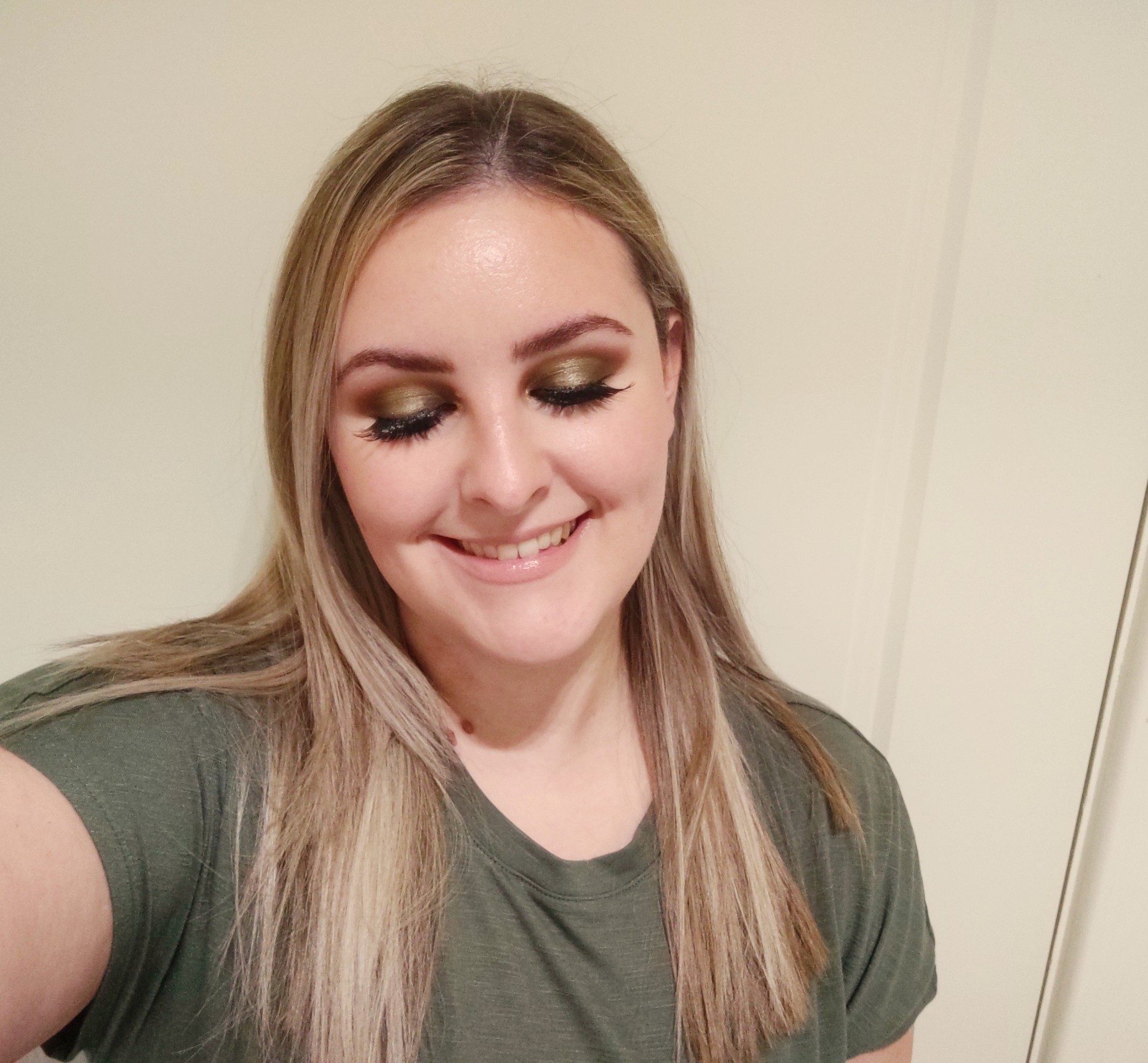 A selfie of Bethany, a woman with long, dark blond hair, smiling with her eyes closed to show off shimmery olive green eye makeup and long, thick eyelashes.