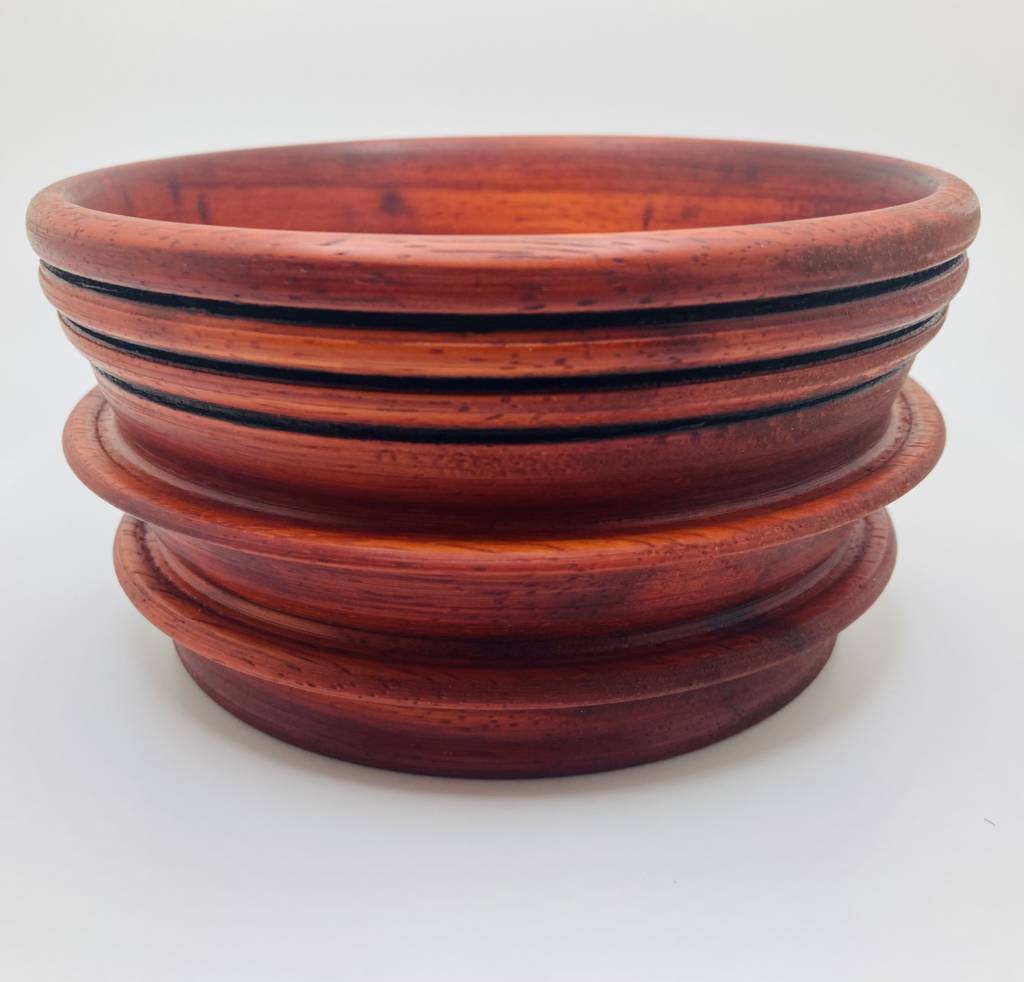 A deep, cherry-colored wooden bowl with multiple tiers and grooves carved along its outside