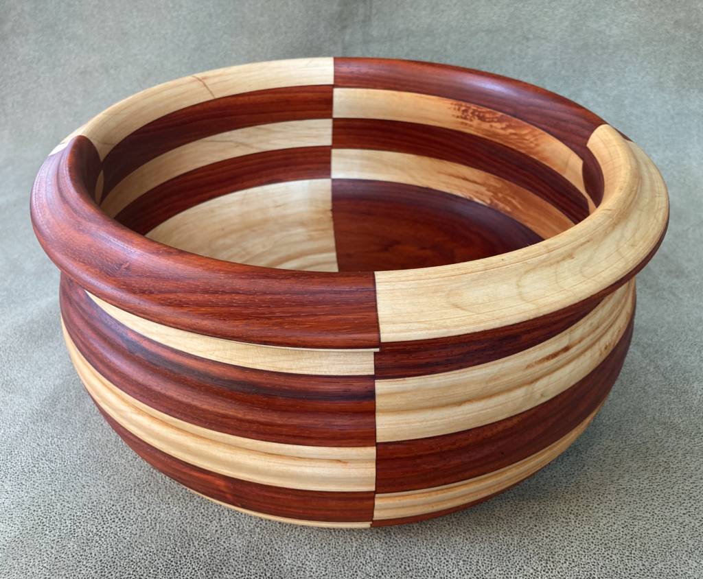 A deep wooden bowl made with alternating stripes of dark and light wood