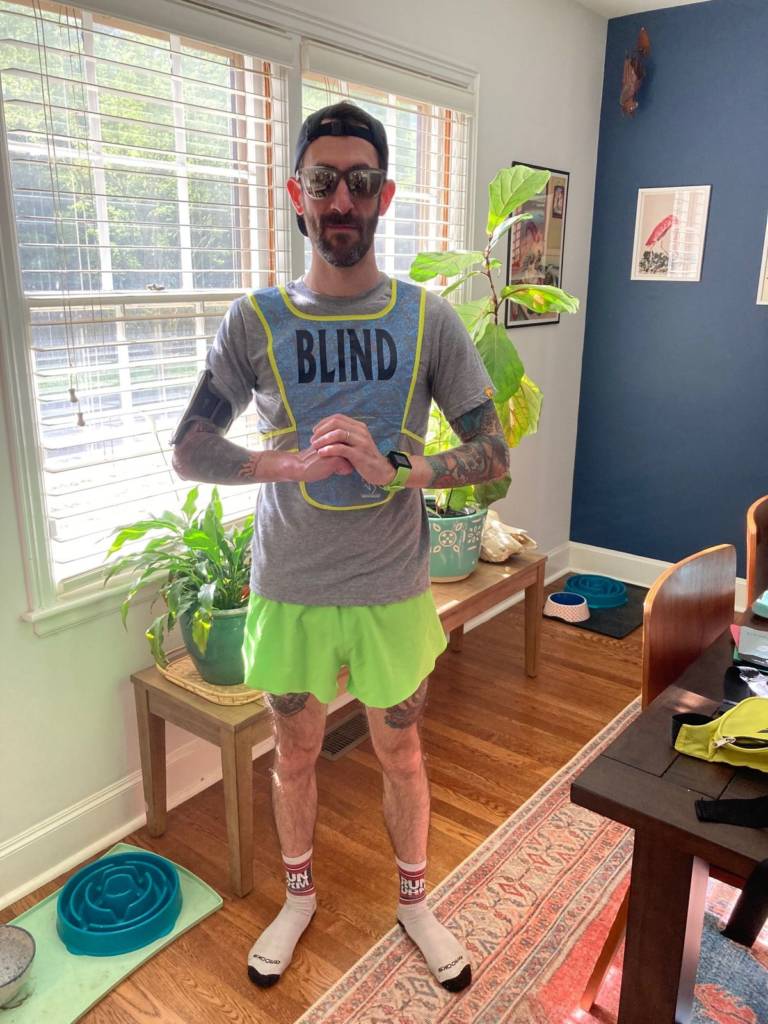 Richie Kahn, in dark glasses and a backwards baseball cap, is ready for a run in athletic gear and a bib that reads "Blind."