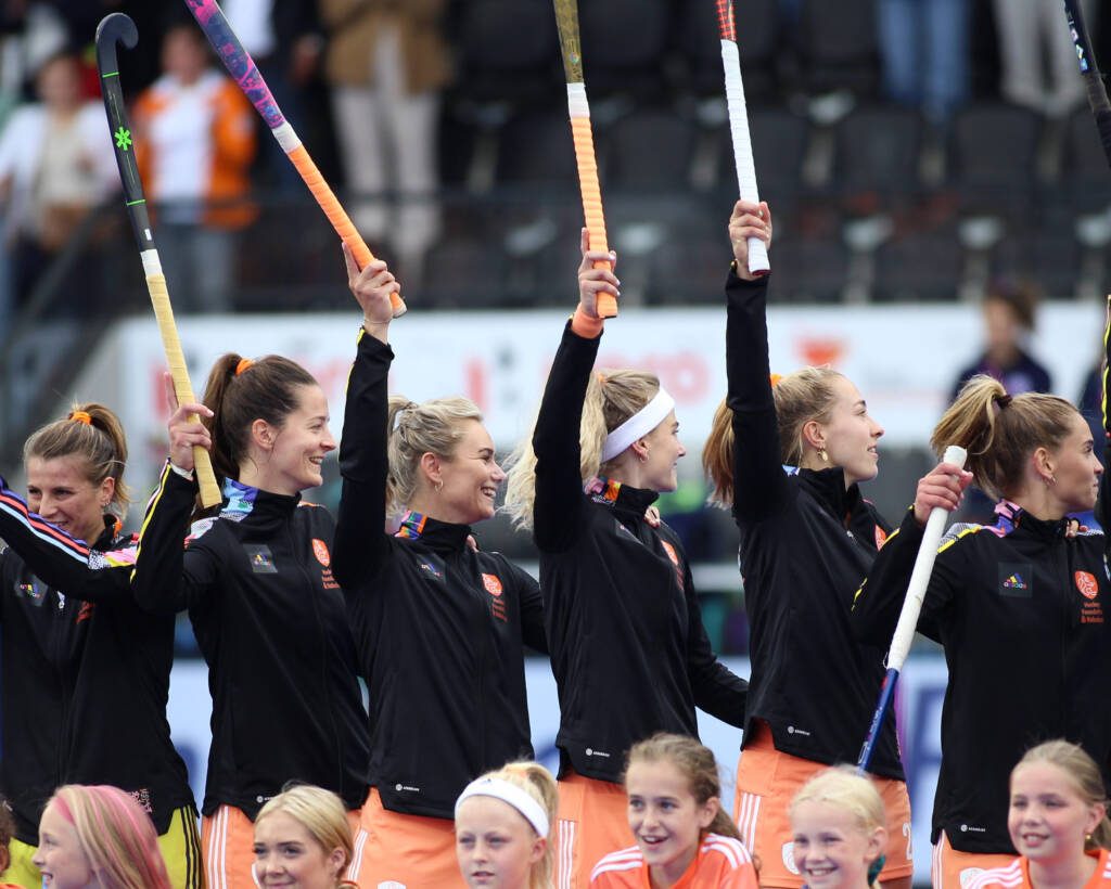 A group of women holding field hockey sticks high in the air, smiling and waving to fans
