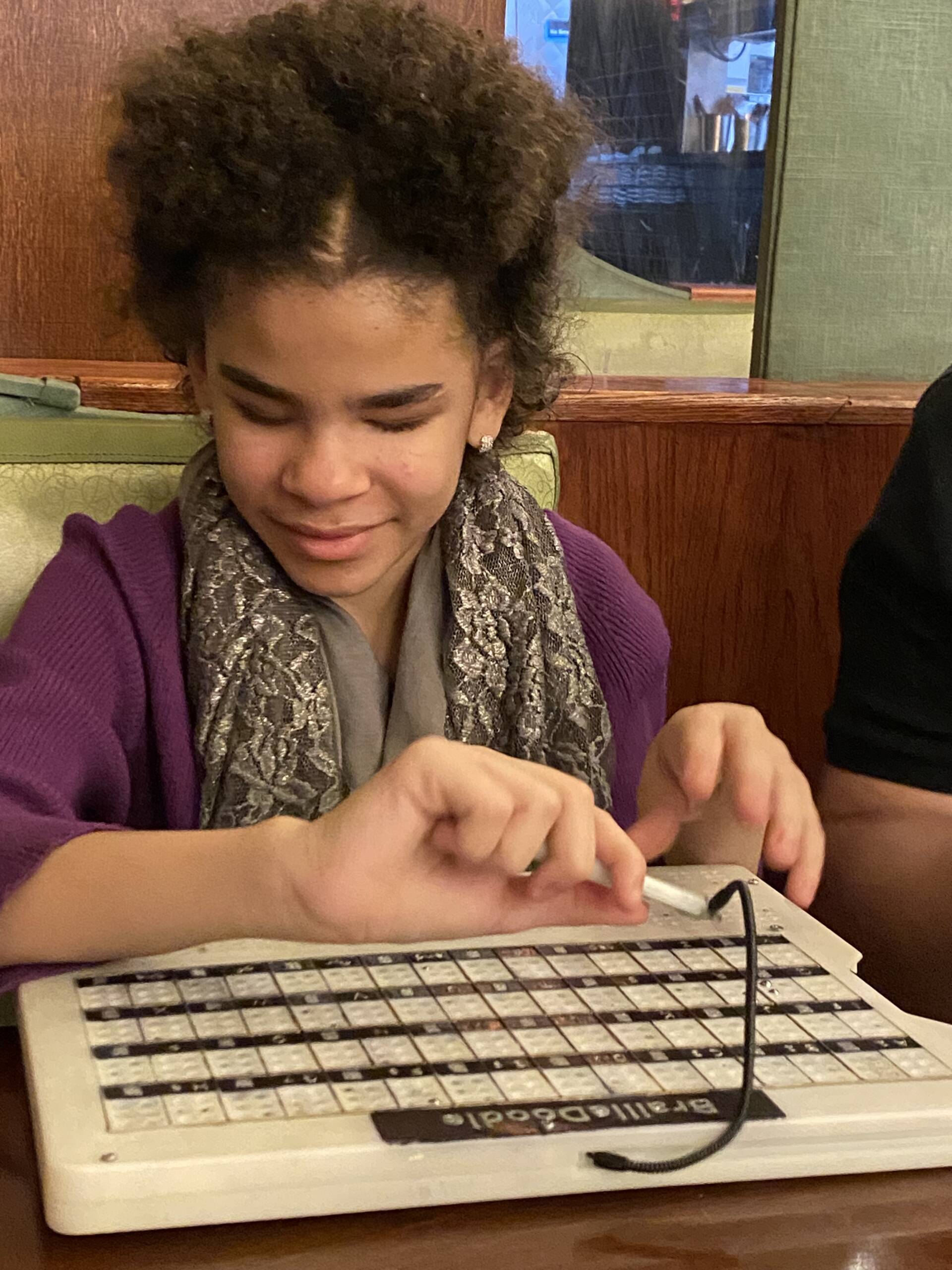 Millie, a 12-year-old Black girl, smiles while using her BrailleDoodle device