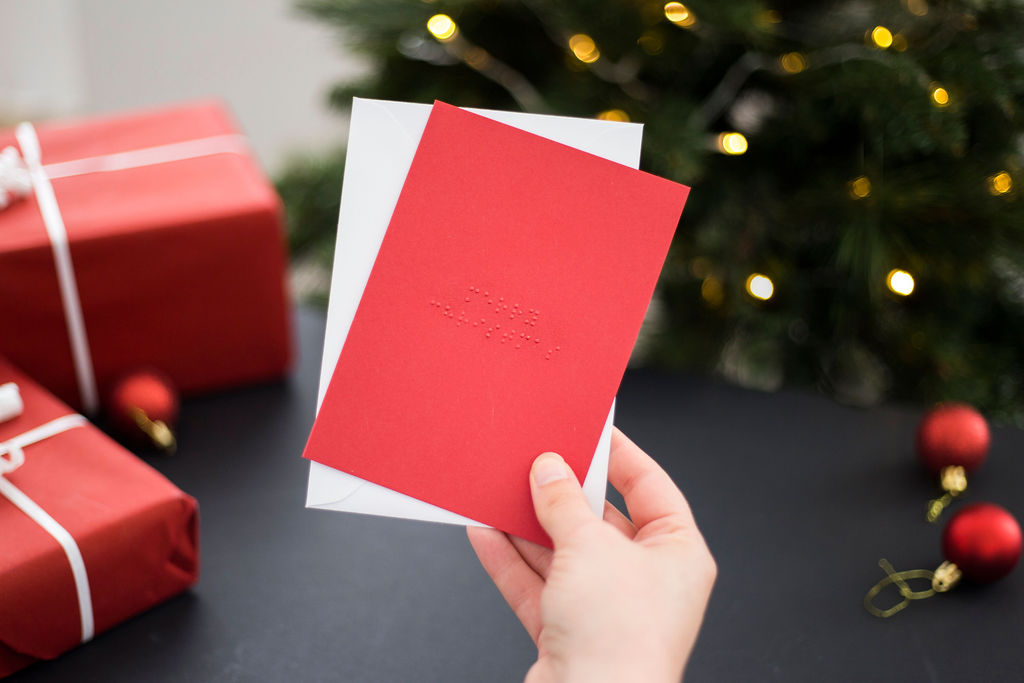 A braille Christmas card on red stock with "Merry Christmas" brailled on the front