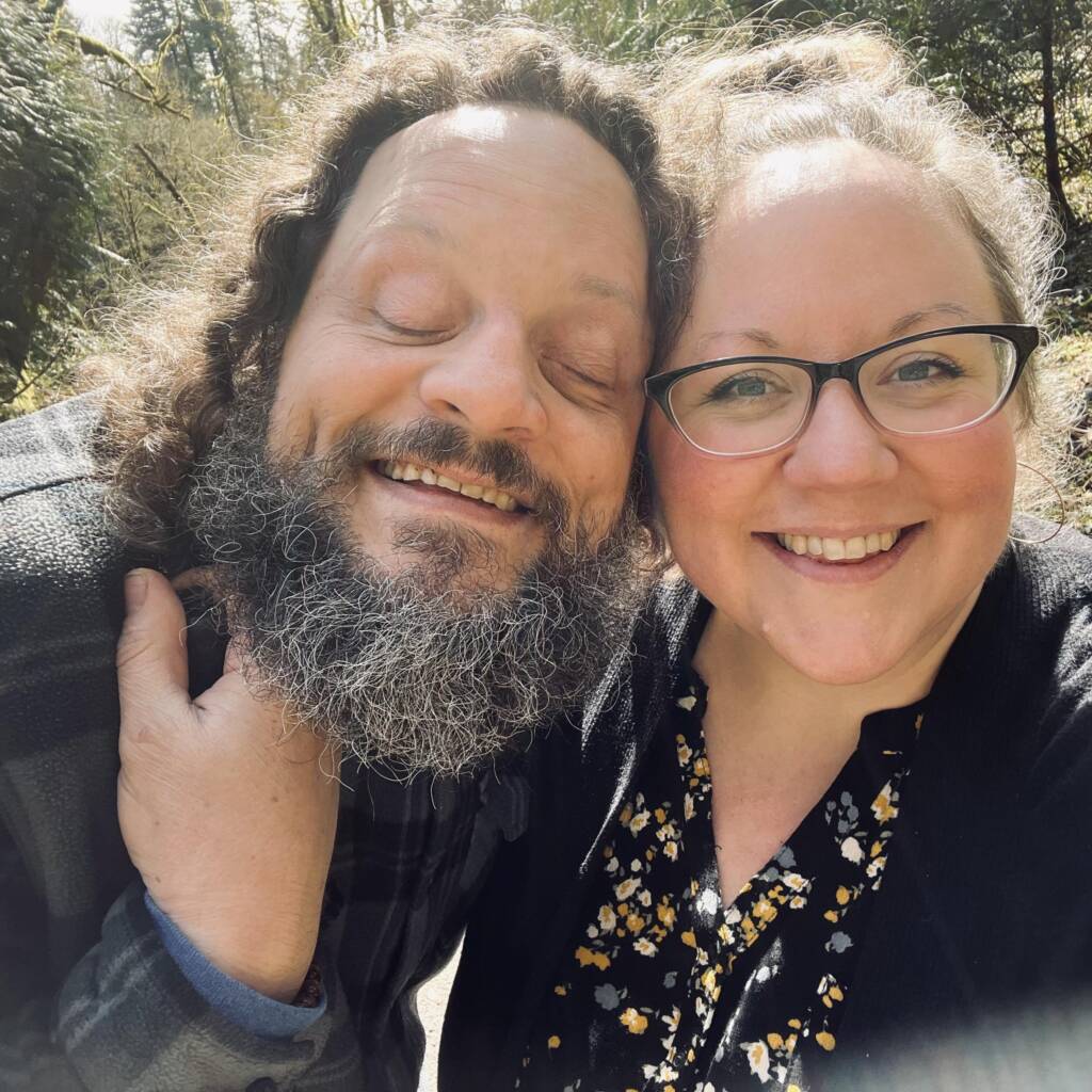 Anni and her husband, John Furniss, the Blind Woodsman, hugging and smiling in a selfie-style photo