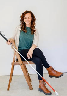 Cane Kids author Kristen Lang poses, perched on a chair holding a white mobility cane