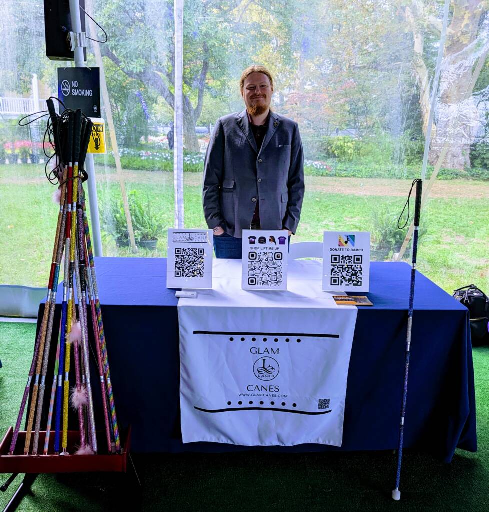 Arthur Gwynne, founder of Glam Canes, stands behind a display table surrounded by sparkly canes