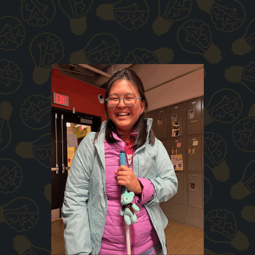 Tina, a young Asian woman, smiles while holding her white cane (complete with teal teddy bear charm dangling from the handle)