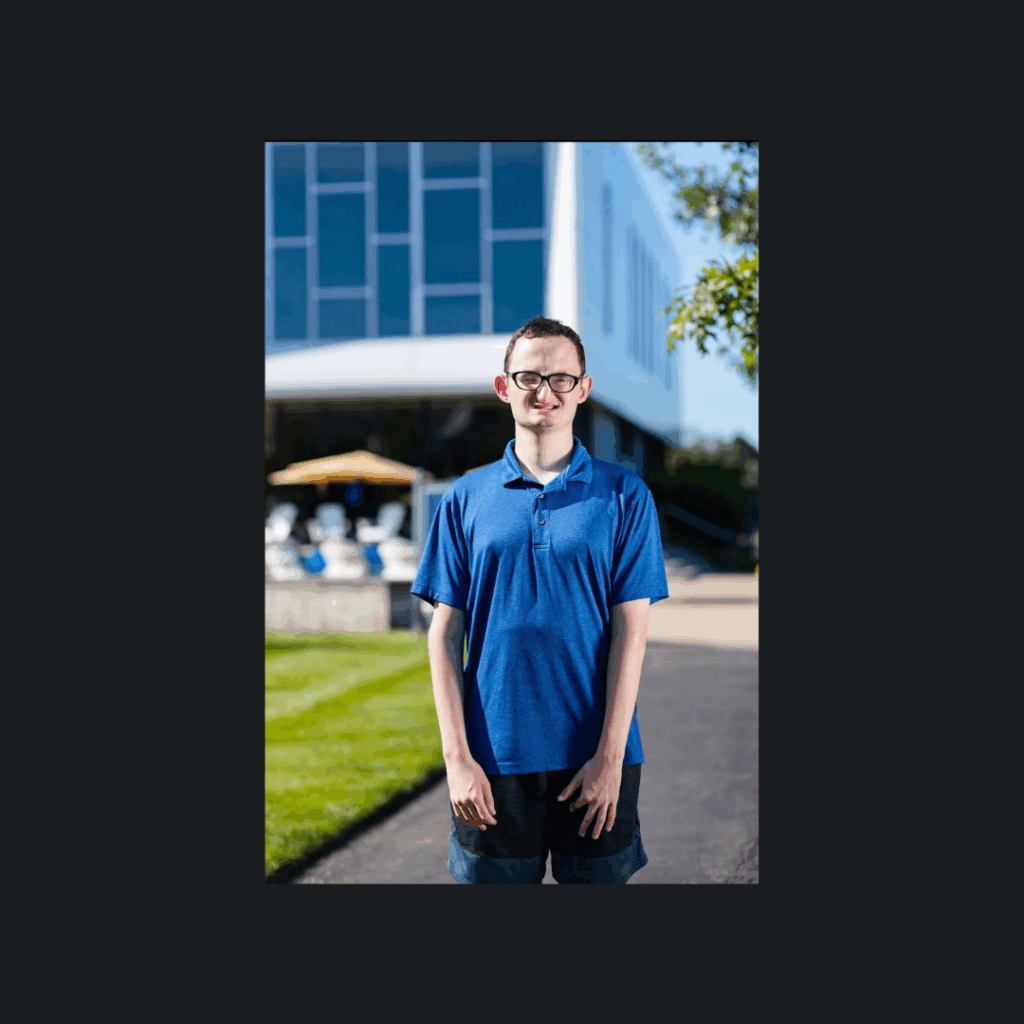 Tom, a young man with short, dark hair, stands outdoors smiling
