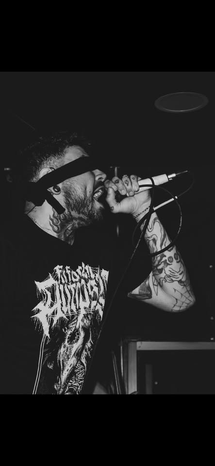 A black-and-white photo of Joel performing on stage, wearing a dark blindfold over his eyes and holding the mic close to his mouth