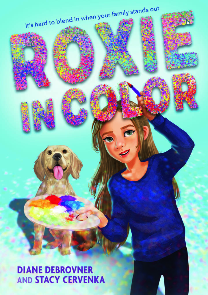 The cover of Roxie in Color: a young girl holding a palette paints the title of the book as a guide dog looks on from behind her. Text: "It's hard to blend in when your family stands out."